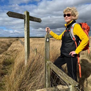 Catriona standing at a stile, on a lovely bright day.