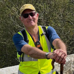 Nick Corble in hi-viz, cap and sunglasses, with walking stick.